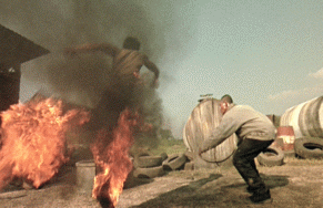 Guy dodges flames near burning barrels—wild action shot